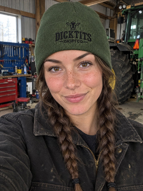 Dicktits Dairy Co. på olivgrön Hatitude Beanie, buren av en yngre vuxen.