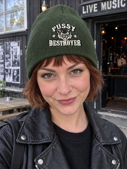 Pussy Destroyer på olivgrön Hatitude Beanie, buren av en yngre vuxen.